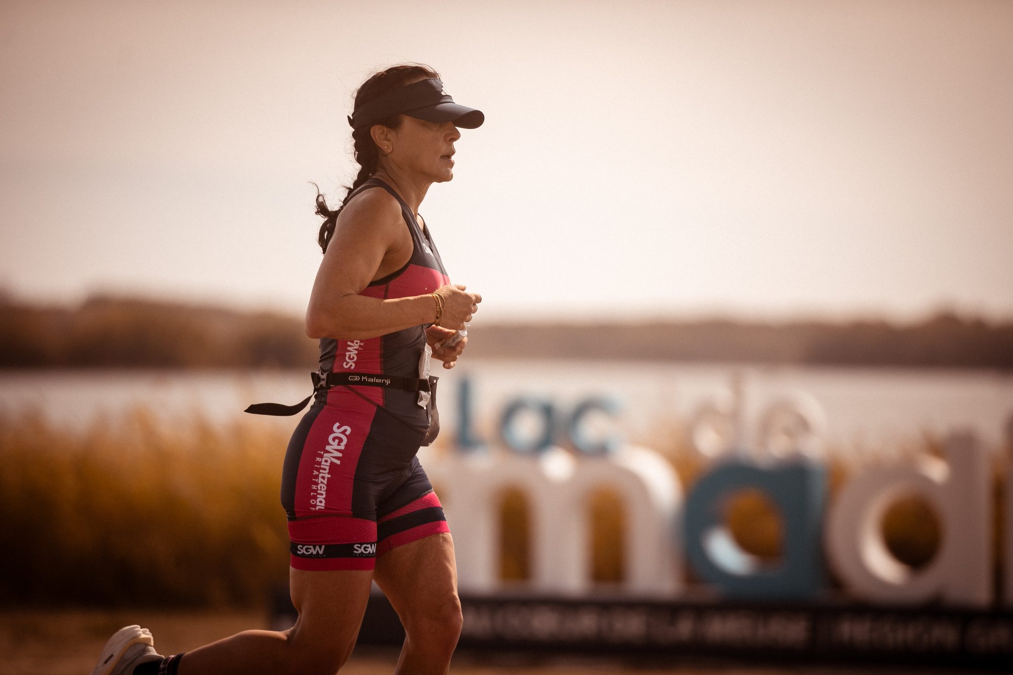 Triathlète en course à pied devant le panneau du Lac de Madine
