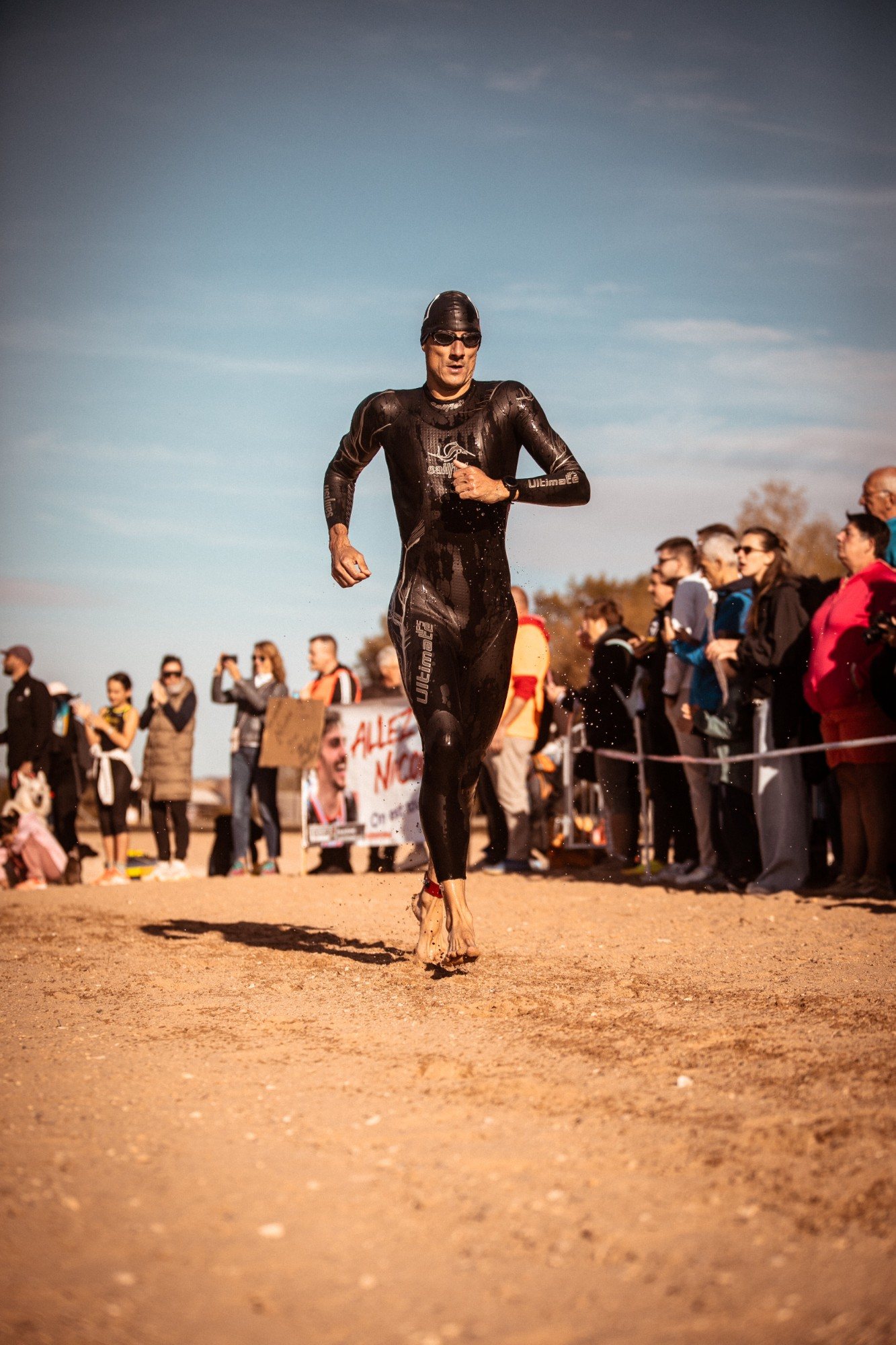 Triathlète qui sort de l'eau en courant sur la plage de Madine, devant les supporters