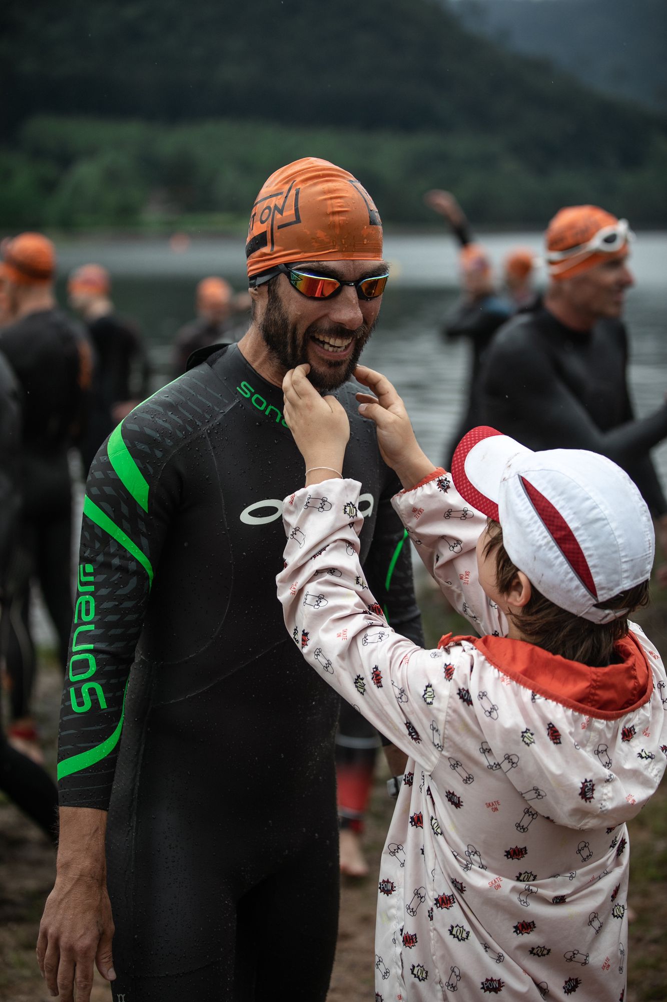 Un enfant ajuste les lunettes d'un triathlète avant le départ natation
